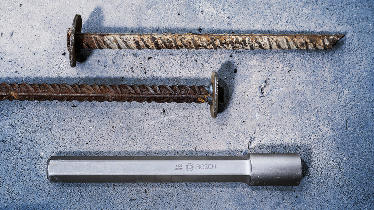 Twee verroeste metalen staven en een stalen beitel liggen op een ruw betonnen oppervlak.