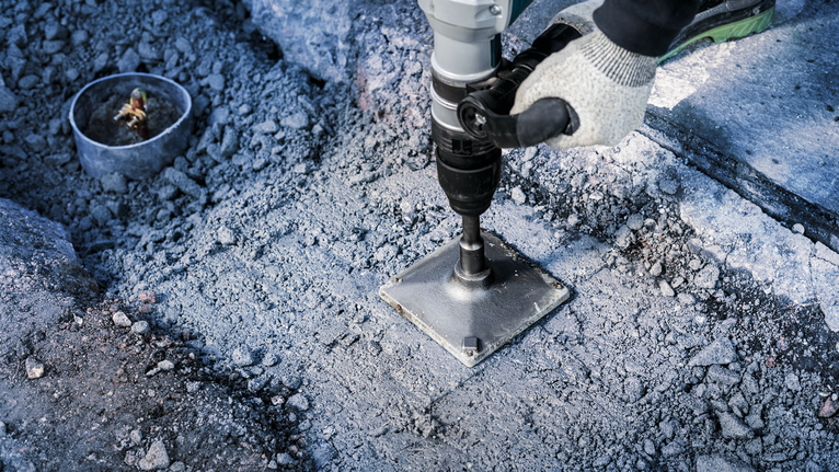 Een persoon die veiligheidsuitrusting draagt, bedient een boormachine op een betonnen oppervlak.