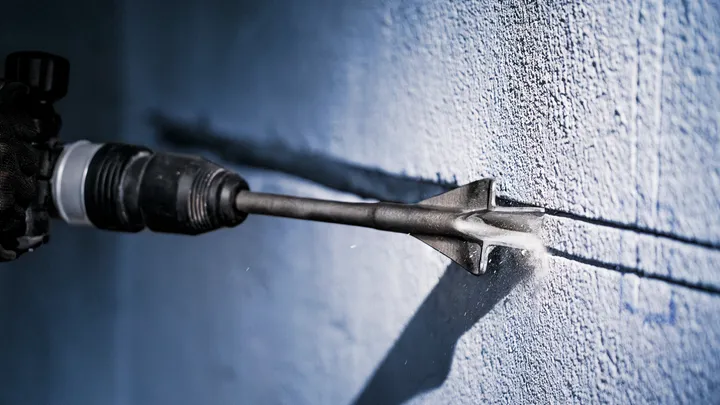 Een persoon die veiligheidsuitrusting draagt, gebruikt een elektrisch gereedschap om een groef in een betonnen muur te kerven.