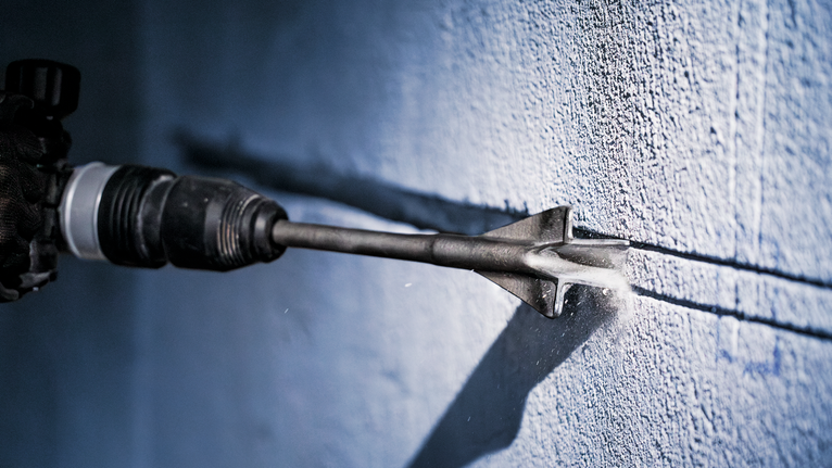 Een persoon die veiligheidsuitrusting draagt, gebruikt een elektrisch gereedschap om een groef in een betonnen muur te kerven.