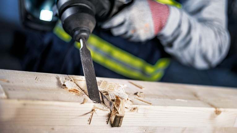 Een persoon die veiligheidsuitrusting draagt, beitelt hout met een elektrisch gereedschap.