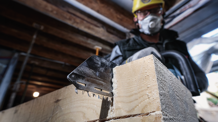Een persoon met veiligheidsuitrusting zaagt dik hout met een elektrische zaag.