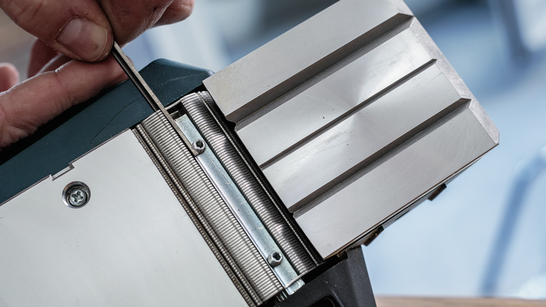 Persoon die een metalen schaafmachineblad met een gereedschap afstelt.