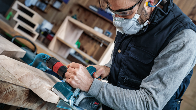 Een persoon die veiligheidsuitrusting draagt, bedient een elektrische zaag om houten planken te zagen.