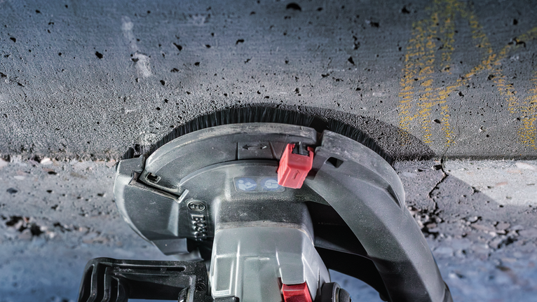 Elektrisch gereedschap schuurt over een betonnen oppervlak, stofborstelbevestiging zichtbaar.
