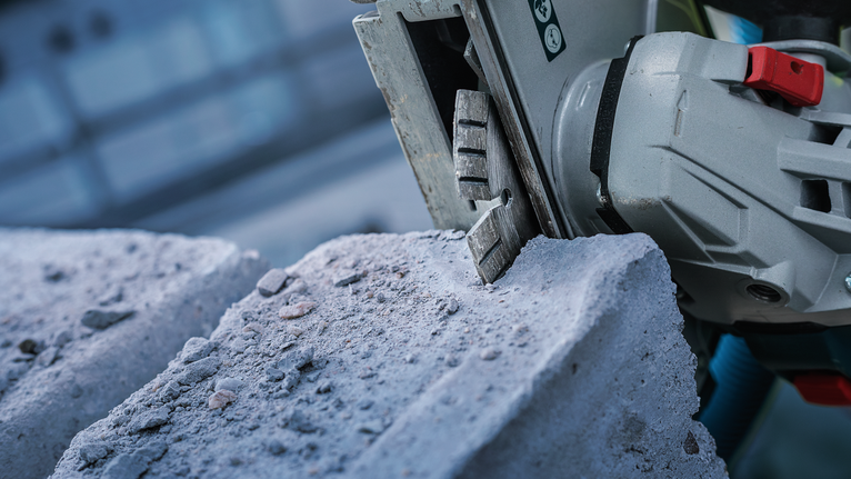 Een elektrisch gereedschap zaagt door een betonblok, waarbij stof vrijkomt.