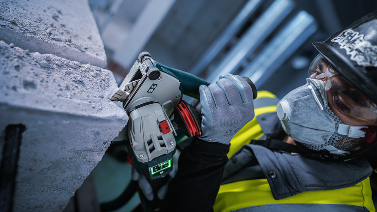 Een persoon die veiligheidsuitrusting draagt, zaagt beton met een elektrisch gereedschap.