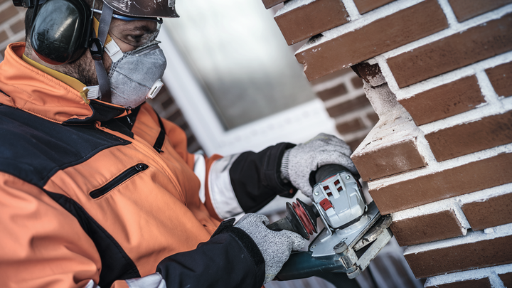 Een arbeider met veiligheidsuitrusting zaagt met behulp van een elektrisch gereedschap groeven in een bakstenen muur.