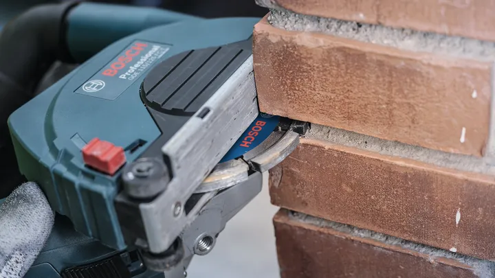 Een persoon die veiligheidsuitrusting draagt, gebruikt een muurfrees om een groef in de baksteen te frezen.