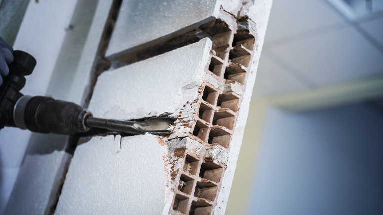 Met een boorhamer wordt een holle bakstenen muur doorgehakt.