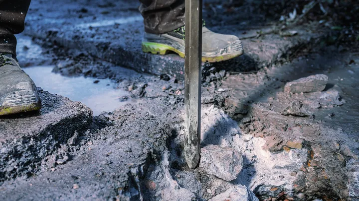 Een persoon die veiligheidsuitrusting draagt, gebruikt een sloopgereedschap om buitenshuis beton te breken.