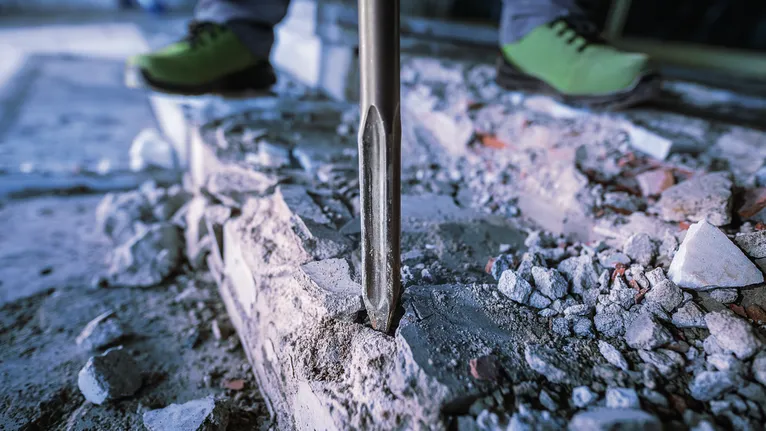 Een persoon die veiligheidsuitrusting draagt, gebruikt een sloopgereedschap om beton te breken.