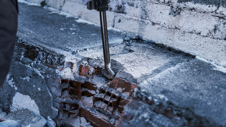 Sloopgereedschap breekt beton op een bakstenen muur.