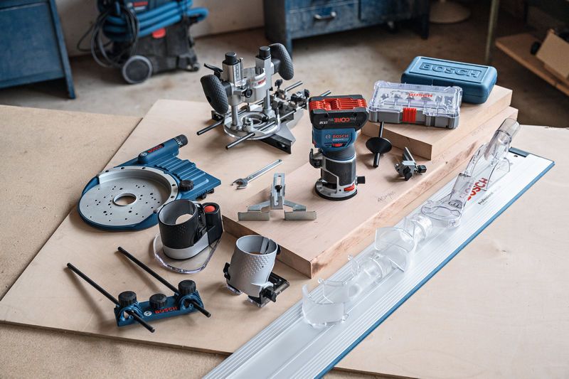 Draadloze bovenfrees met diverse houtbewerkingsaccessoires en hulpstukken op een werkbank.