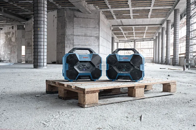 Twee robuuste radio's op een houten pallet in een groot, onafgemaakt gebouw.