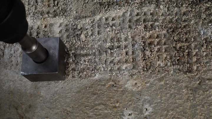 Metalen gereedschap waarmee vierkante inkepingen worden gemaakt in een ruw betonoppervlak.