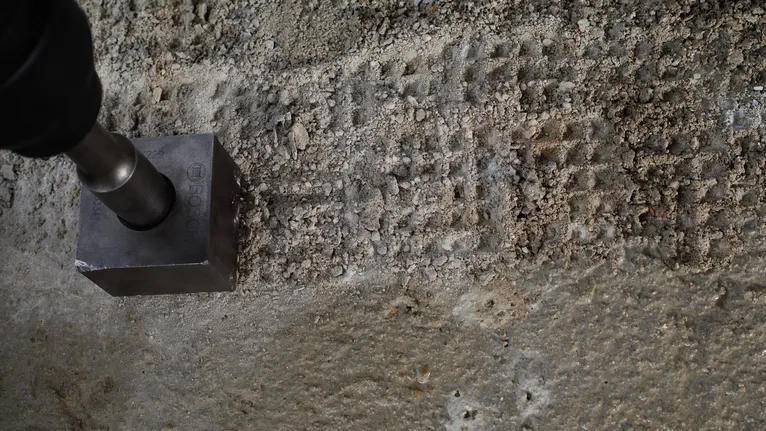 Metalen gereedschap waarmee vierkante inkepingen worden gemaakt in een ruw betonoppervlak.