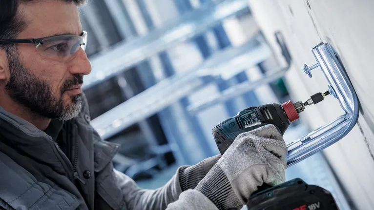 Persoon die veiligheidsuitrusting draagt, installeert metalen beugel met behulp van een accuboormachine.