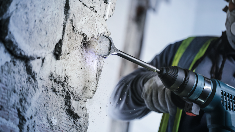 Een persoon die veiligheidsuitrusting draagt, gebruikt een elektrisch gereedschap om beton te bikken.