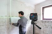 Persoon lijnt tegels op een muur uit met behulp van een laserwaterpasinstrument tijdens een renovatie.