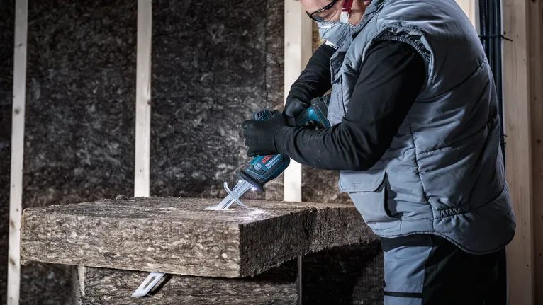 Een persoon met veiligheidsuitrusting zaagt isolatiemateriaal met een elektrische zaag.