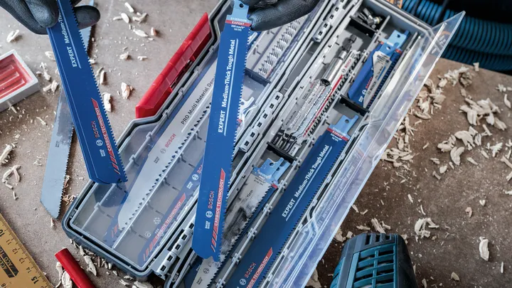 Een persoon die veiligheidsuitrusting draagt, kiest een reciprozaagblad uit een opbergkoffer.