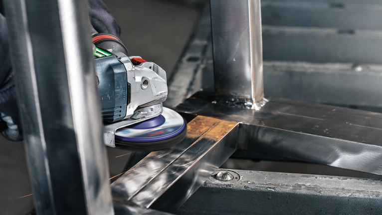 Persoon bedient een haakse slijper om lasnaden op een metalen frame glad te maken.