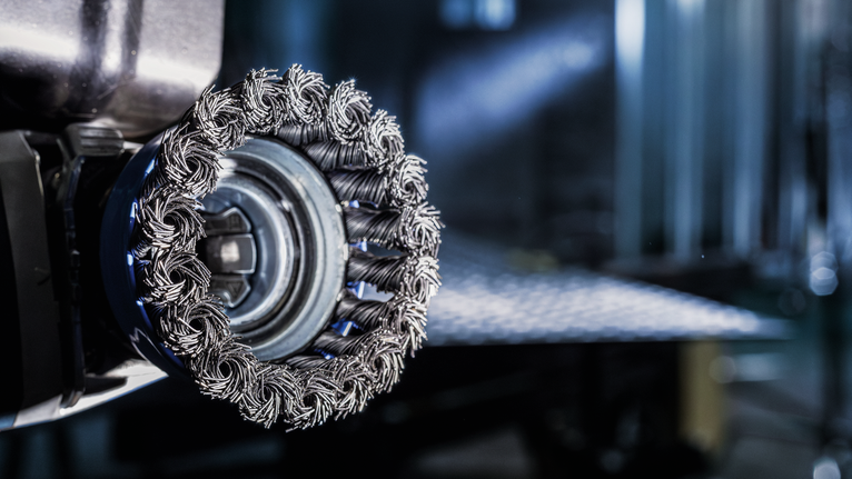 Close-up van een komstaalborstel bevestigd aan een elektrisch gereedschap voor de voorbereiding van metalen oppervlakken.