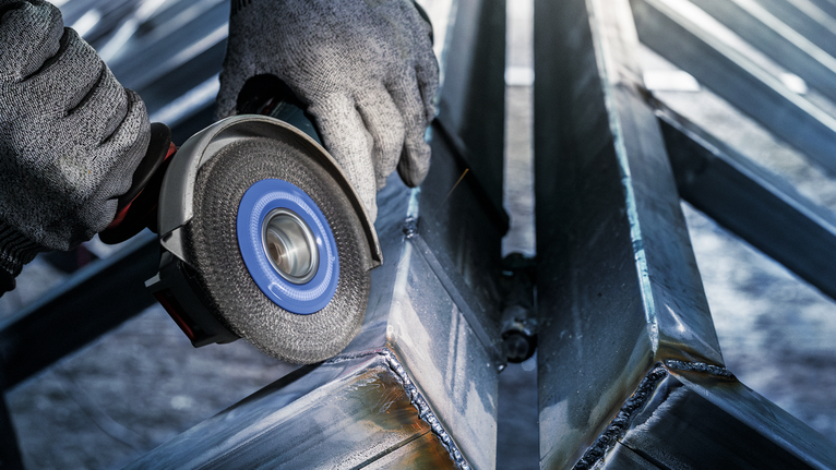 Persoon die veiligheidsuitrusting draagt, slijpt een metalen balk met een elektrisch gereedschap.