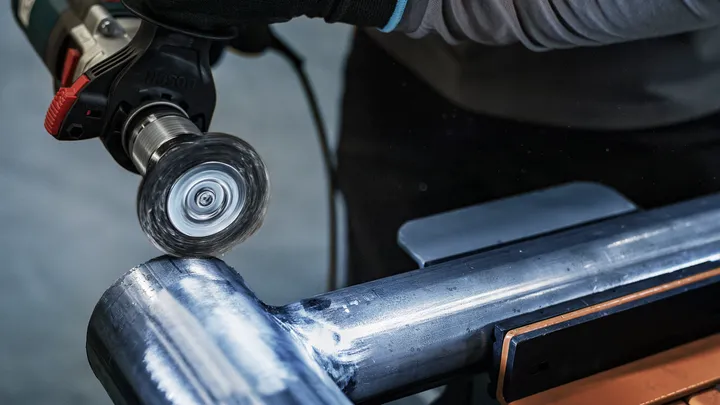 Een persoon die veiligheidsuitrusting draagt, polijst een metalen pijp met een elektrisch gereedschap.