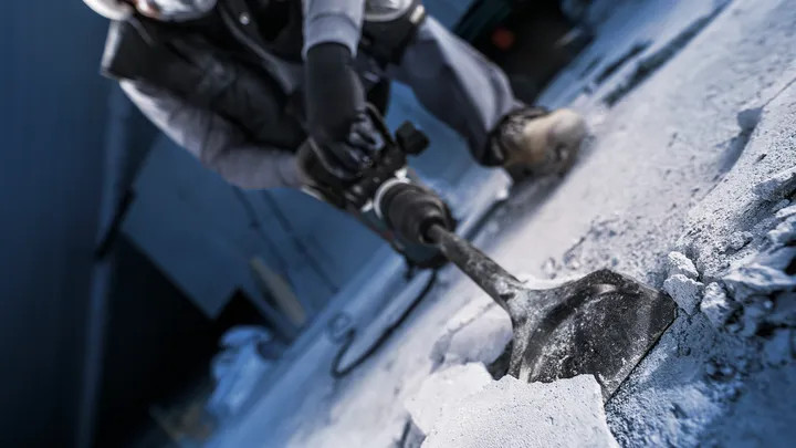 Een persoon met veiligheidsuitrusting breekt beton met een sloopgereedschap.