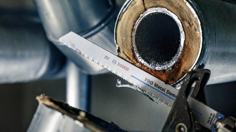 Zaagblad van een reciprozaag dat door een verroeste metalen pijp zaagt.