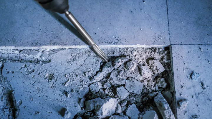 Beitel slaat in een betonnen vloer, waarbij puin en stof ontstaat.