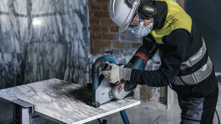 Een persoon met veiligheidsuitrusting zaagt een marmeren plaat met een elektrisch gereedschap.