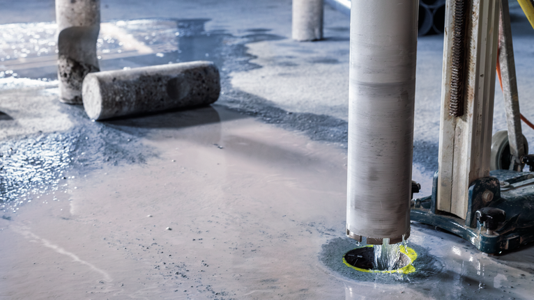 Kernboormachine maakt een cirkelvormige snede door nat beton op een bouwvloer.