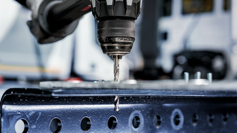 Elektrische boormachine maakt een gat in een metalen balk.