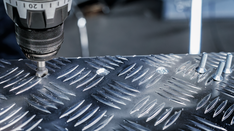 Boor een schroef door een metalen plaat met structuur.
