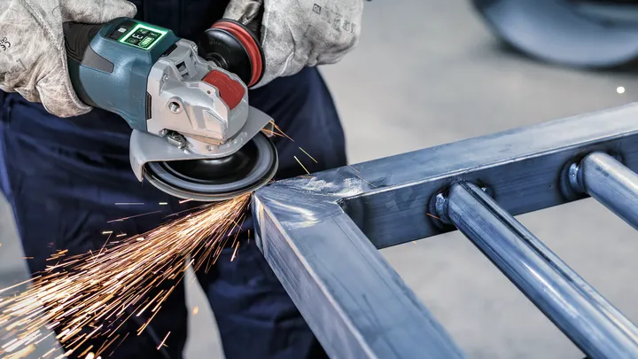 Een persoon die veiligheidsuitrusting draagt, schuurt tegen een metalen frame, waardoor felle vonken ontstaan.