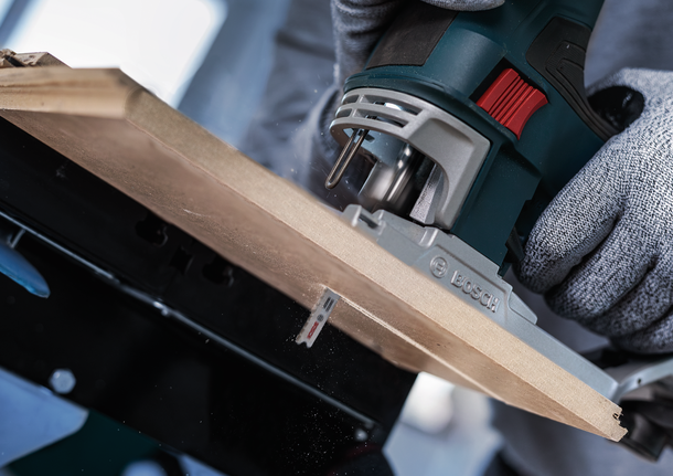 Een persoon die veiligheidsuitrusting draagt, gebruikt een decoupeerzaag om een houten plank te zagen.