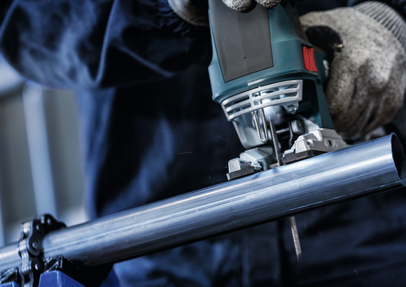 Een persoon die veiligheidsmateriaal draagt, gebruikt een decoupeerzaag om een metalen pijp door te zagen.