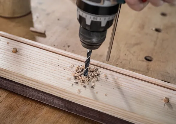 Persoon boort een gat in een houten plank.