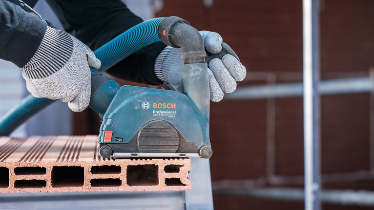 Een persoon met veiligheidsuitrusting schuurt een bakstenen blok met een elektrisch gereedschap.
