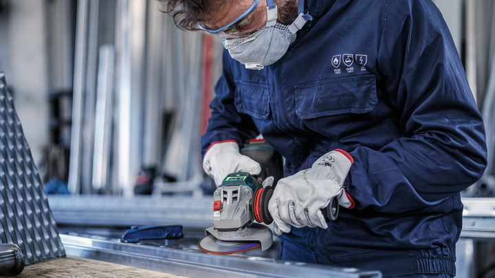 Persoon die veiligheidsuitrusting draagt, slijpt een metalen balk met een elektrisch gereedschap.
