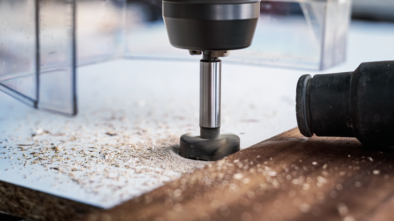 Roterend gereedschap waarmee een gat in een houten oppervlak wordt gemaakt met verspreide houtsnippers.