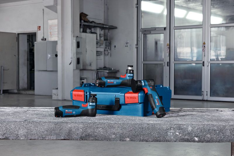 Accu-excenterschuurmachines en een blauwe koffer op een betonnen oppervlak in een werkplaats.