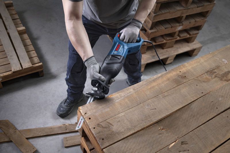 Een persoon die veiligheidsuitrusting draagt, gebruikt een reciprozaag om een houten pallet te zagen.