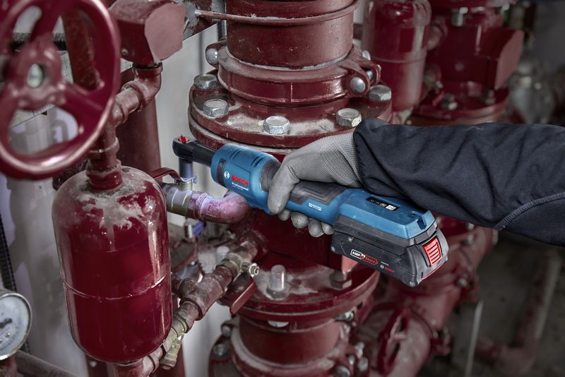 Een persoon die veiligheidsuitrusting draagt, gebruikt een snoerloze ratelsleutel op industriële leidingen.