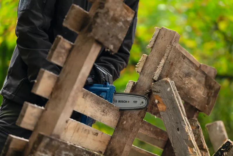 Een persoon met veiligheidsuitrusting zaagt houten planken met behulp van een snoerloze snoeizaag.