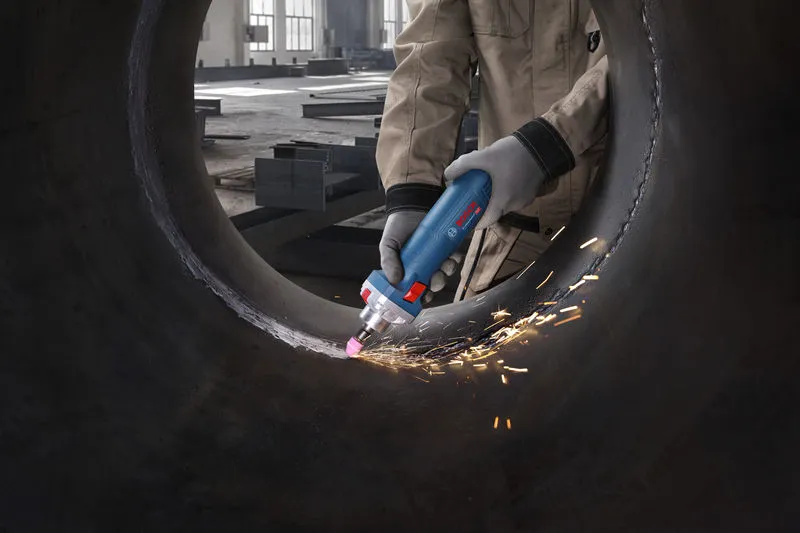 Een persoon met veiligheidsuitrusting slijpt de binnenkant van een grote metalen pijp met een rechte slijper.