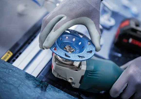 Een persoon die veiligheidsuitrusting draagt, bevestigt een slijpschijf aan een elektrisch gereedschap.